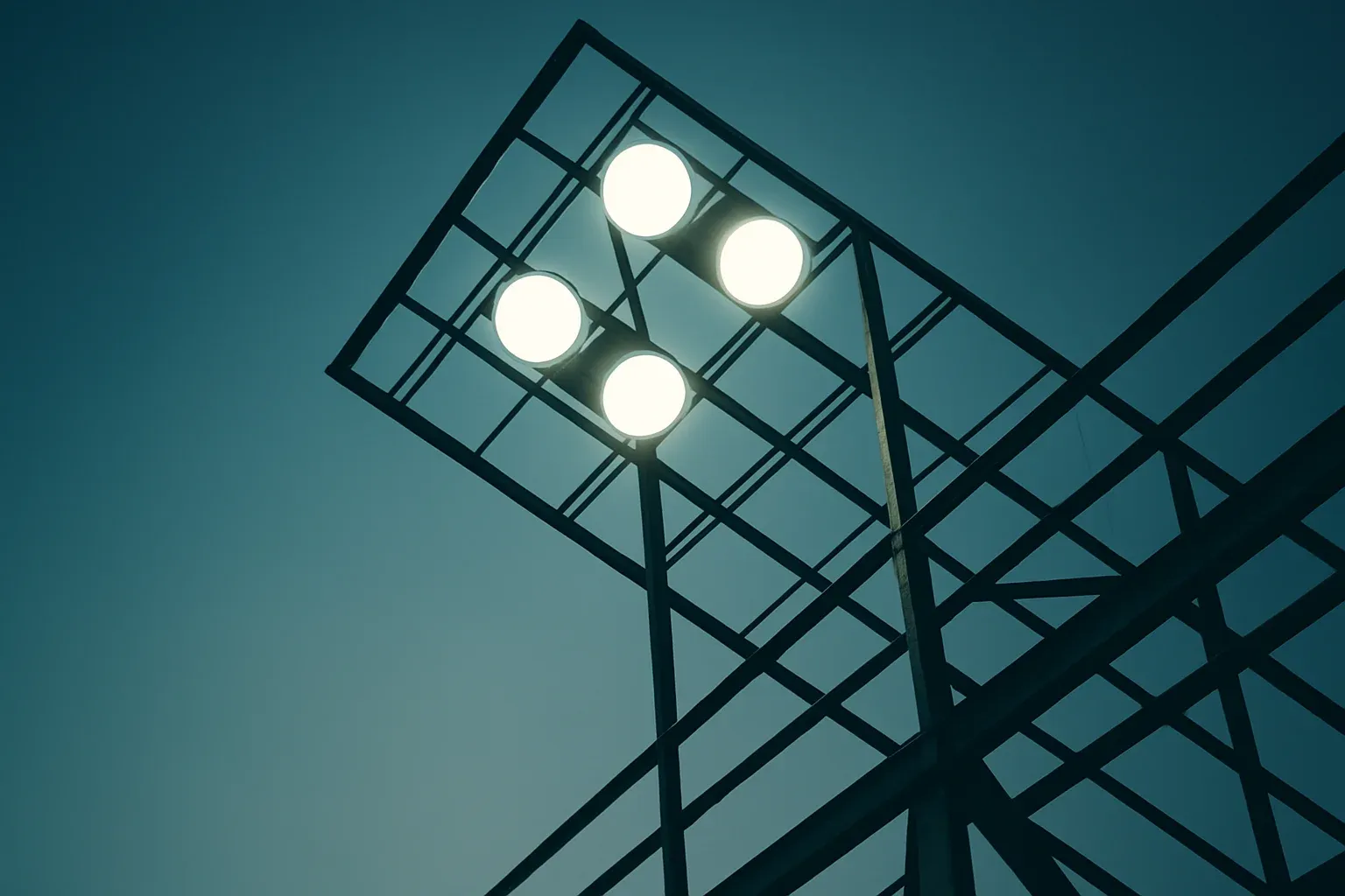 Four bright stadium lights viewed through metal structure at dusk